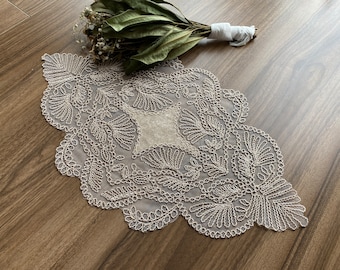 May include: A delicate white lace doily with a floral design. The doily is made of a fine, sheer fabric and has a scalloped edge.