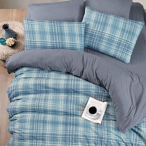 Può includere: Un copripiumino a quadri blu e bianchi con un cuscino grigio e un cuscino decorativo grigio. Il copripiumino è su un letto con pavimento in legno.