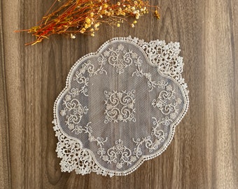 May include: A white lace doily with a delicate floral pattern. The doily is circular with a scalloped edge and is made of a fine, sheer fabric.