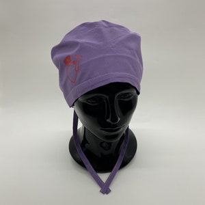 Può includere: Cappello chirurgico viola con un design a forma di cuore rosso e stetoscopio.