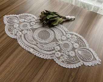 May include: White crocheted table runner with intricate floral and geometric designs. The runner is made of delicate lace and has a scalloped edge.