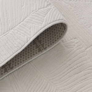 May include: Close-up of a white rug with a textured leaf pattern. The rug has a brown backing with the word "merino" printed on it.