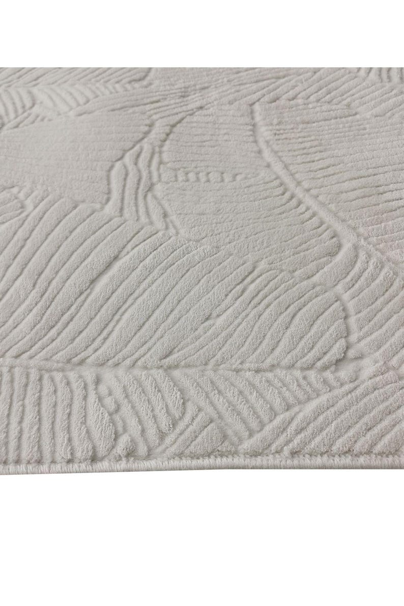 May include: White area rug with a textured, embossed pattern of leaves. The rug has a subtle sheen and a soft, plush feel.
