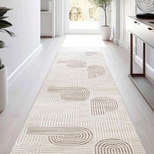 Può includere: Un tappeto rettangolare beige e marrone con un motivo geometrico. Il motivo del tappeto è composto da linee curve e rette, creando un motivo astratto. È posizionato su un pavimento in legno chiaro in un corridoio.