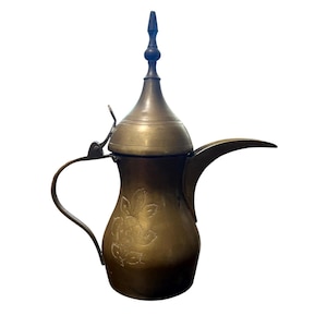 May include: A vintage brass coffee pot with a long spout and a curved handle. The pot features an ornate floral design on the body and a decorative finial on the lid. The pot is a warm, antique gold color.