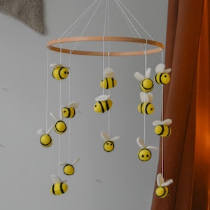 May include: A handmade baby mobile featuring a wooden hoop and numerous felt bees in yellow and black. The bees are suspended by white strings, creating a whimsical nursery decoration. The mobile includes a wooden bead at the top.