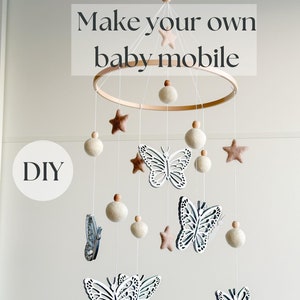 Può includere: Mobile per neonati fai-da-te con un anello di legno, palline di feltro bianche, stelle di legno e farfalle. Il mobile è appeso al soffitto.