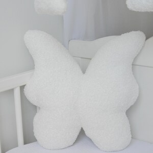 Puede incluir: Almohada blanca y esponjosa con forma de mariposa para una cuna de beb&eacute;.