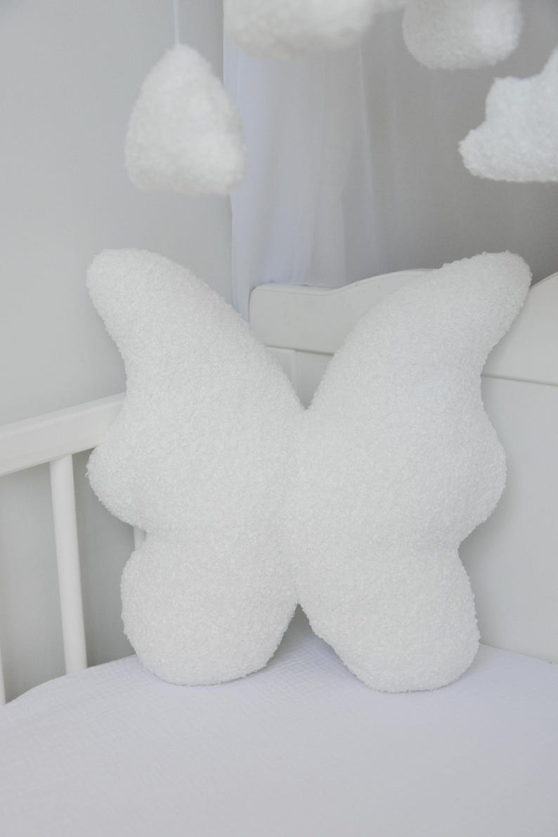 Puede incluir: Almohada blanca y esponjosa con forma de mariposa para una cuna de beb&eacute;.