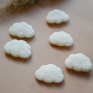 Może przedstawiać: Sześć białych filcowych kształtów chmur na jasnobrązowym tle.