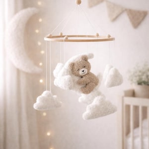 May include: A baby mobile featuring a plush teddy bear nestled on fluffy white clouds. The mobile is suspended from a wooden ring with a simple design, creating a whimsical nursery decoration. The color palette is soft and neutral.