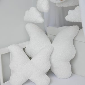 Puede incluir: Dos almohadas blancas y esponjosas con forma de nube en una cuna. Las almohadas est&aacute;n hechas de un material suave y afelpado y tienen forma de nubes. Las almohadas est&aacute;n dispuestas en forma de cruz.