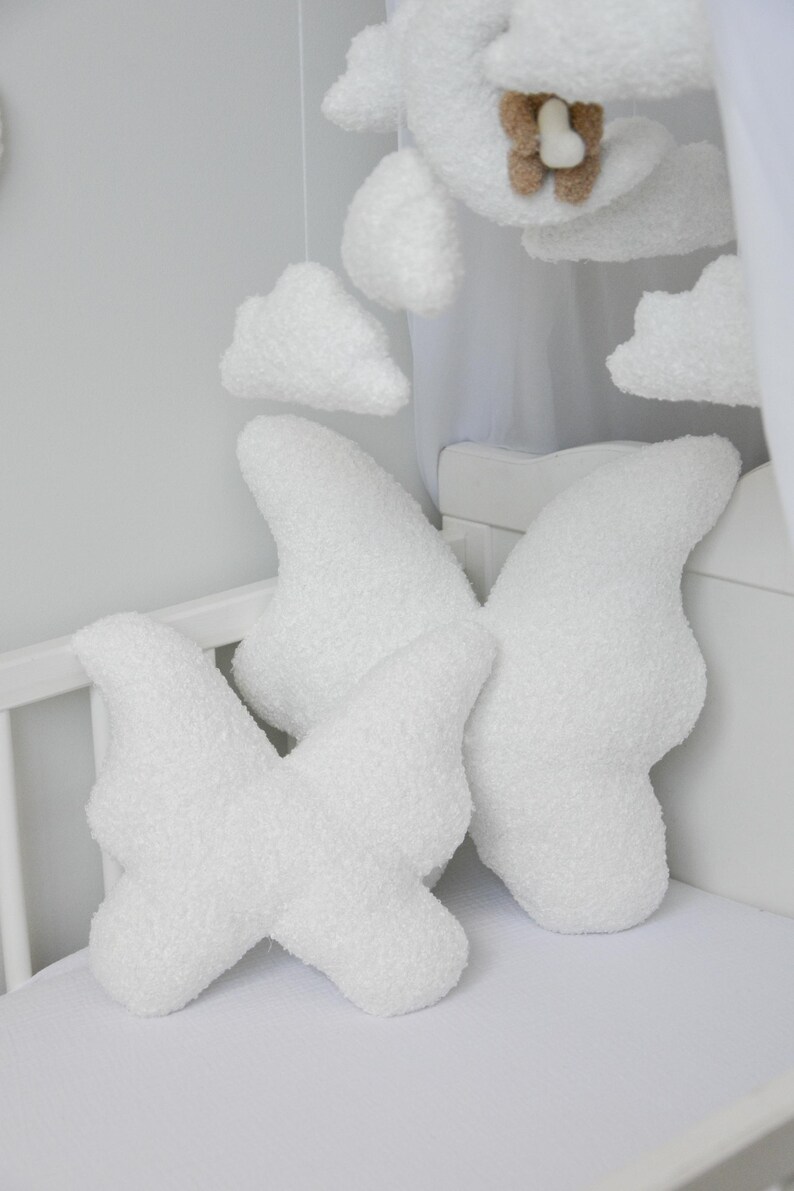 Puede incluir: Dos almohadas blancas y esponjosas con forma de nube en una cuna. Las almohadas est&aacute;n hechas de un material suave y afelpado y tienen forma de nubes. Las almohadas est&aacute;n dispuestas en forma de cruz.