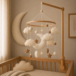 Peut inclure: Mobile pour bébé en bois avec des nuages, des étoiles et des lunes en feutre suspendus au-dessus d'un lit bébé. Le mobile est suspendu à un bras en bois fixé au lit. Une grande lune en croissant décore le mur.