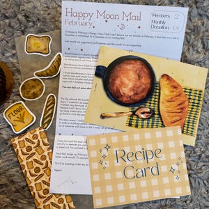 Puede incluir: Un surtido de artículos de papelería, que incluyen una tarjeta de recetas, pegatinas y un boletín informativo titulado "Happy Moon Mail February". La tarjeta de recetas tiene un patrón de cuadros amarillos. Las pegatinas representan pan y harina.