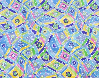 May include: A colorful fabric with a wavy pattern. The design features a mosaic of shapes in shades of blue, green, yellow, purple, and pink. Small floral and dot motifs are scattered throughout the pattern. The fabric is on a cutting mat with inch measurements.