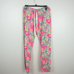 May include: Gray leggings with a vibrant floral pattern in shades of pink, yellow, and teal. The leggings have a drawstring waist and are hanging on a black hanger. The floral print is dense and covers the entire surface of the leggings.