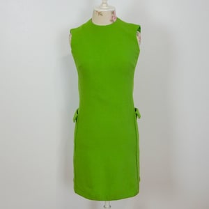 May include: A sleeveless, lime green dress with a straight silhouette. The dress has small decorative bows on each side near the waist. The dress is displayed on a mannequin against a plain white background, showcasing its simple, yet stylish design.
