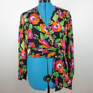 Puede incluir: Un top envolvente negro con mangas largas, con un vibrante estampado floral en naranja, morado y verde. El top se ata a la cintura y se muestra en un maniquí azul, mostrando su diseño.
