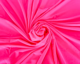 May include: Bright pink fabric arranged in a spiral pattern. The fabric is smooth and appears to be a lightweight material, with folds and shadows creating depth and texture. The color is a vibrant, saturated pink.