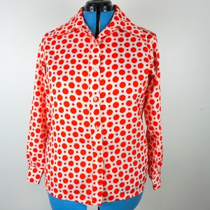 May include: A button-down shirt with a white background and large red polka dots. The long-sleeved shirt has a collar and is buttoned up. The shirt is displayed on a blue dress form.
