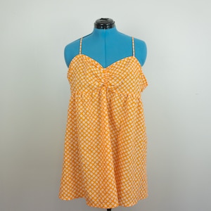 May include: An orange sundress with a white floral pattern is displayed on a blue mannequin. The dress features thin spaghetti straps and a gathered bodice. The fabric is lightweight, and the dress has a flowing, A-line skirt.