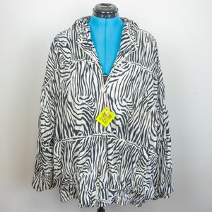 May include: A black and white zebra print jacket with a zipper closure. The jacket is displayed on a blue dress form. The jacket has a collar and long sleeves. A yellow tag with a QR code hangs from the zipper.