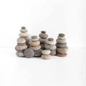 Puede incluir: Una colección de piedras grises, marrones y blancas apiladas en una formación equilibrada sobre una superficie blanca. Las piedras están dispuestas en fila, y cada pila se hace progresivamente más alta.