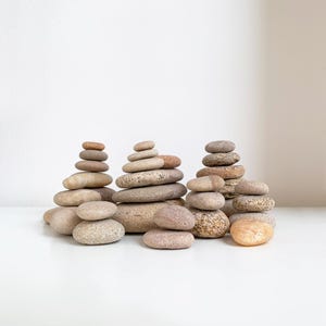 May include: A group of stacked smooth stones in various shades of brown and gray, arranged in a zen-like formation on a white surface.