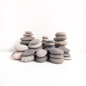 Puede incluir: Una colección de piedras grises y marrones apiladas en varias formaciones sobre una superficie blanca. Las piedras son lisas y redondeadas, creando un ambiente zen.