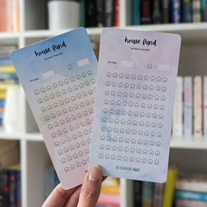 May include: Two house fund savings tracker cards with a watercolour background. The cards have a space to write in your savings goal and a grid of 100 small house icons to colour in as you save.