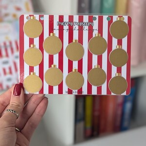 May include: A red and white striped card with gold circles. The card has the text "Merry Mystery Saving Challenge" on it.