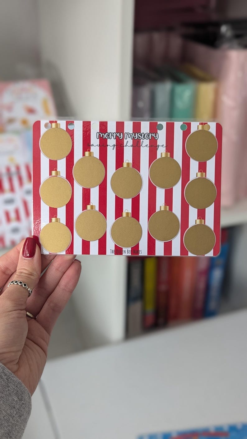 May include: A red and white striped card with gold circles. The card has the text "Merry Mystery Saving Challenge" on it.