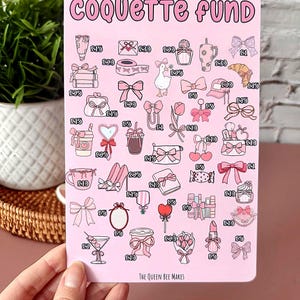 May include: A pink sticker with the words "COQUETTE FUND" in a bubble font. The sticker features illustrations of bows, shoes, and other feminine items. The text "THE QUEEN BEE MAKES" is at the bottom.
