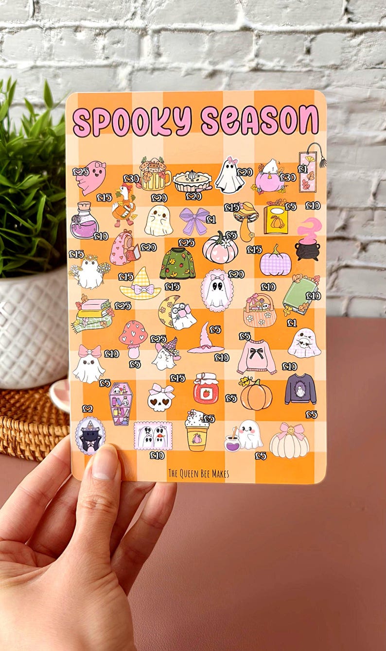 May include: A rectangular sticker sheet with a checkered orange background and the words "SPOOKY SEASON" at the top. The sheet features various Halloween-themed illustrations, including ghosts, pumpkins, and sweaters. The Queen Bee Makes is printed at the bottom.