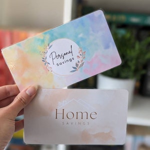 May include: Two colourful cards with watercolour backgrounds. The top card has a light blue, yellow, and pink background with a circle that says "Personal Savings". The bottom card has a light peach background with the text "Home Savings".