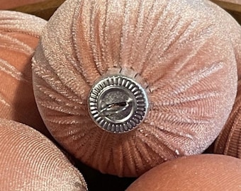 May include: Close-up of several peach-colored velvet Christmas ornaments. Each ornament has a ribbed texture and a silver metal cap. The ornaments are clustered together, suggesting a holiday or seasonal theme.