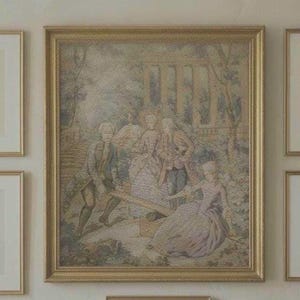 May include: A framed tapestry depicting a historical scene with figures in period clothing. The artwork features a group of people near a seesaw, with a building and trees in the background. The frame is gold.