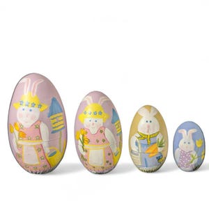 May include: Four Easter egg-shaped nesting dolls. The dolls are painted with pastel colors and feature bunny characters wearing hats and aprons. The largest doll is light pink, and the smallest is light blue. The dolls are decorative.