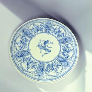 May include: A white ceramic plate with a blue and white floral design. The plate features a repeating pattern of holly leaves and berries.