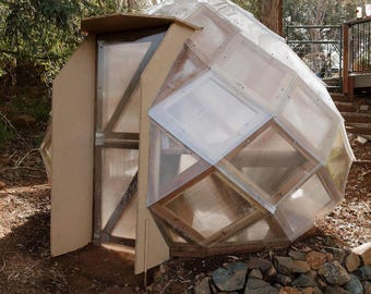 May include: A small, geodesic dome-shaped structure made of wood and clear plastic panels. The dome has a wooden door and is surrounded by rocks.