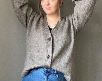 May include: A gray knitted cardigan with a v-neck and button closure. The cardigan is worn over a pair of blue jeans.