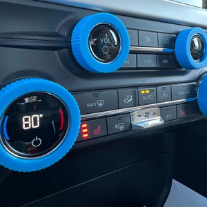 May include: Blue knob covers for car controls, with a digital display showing 80 degrees. The knobs have a textured surface and are labelled "VOL", "MAX", "AUTO", "MAX A/C", and "DUAL".