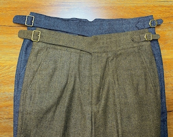 May include: A pair of brown and blue tweed pants with a herringbone pattern. The pants have two adjustable straps with brass buckles.