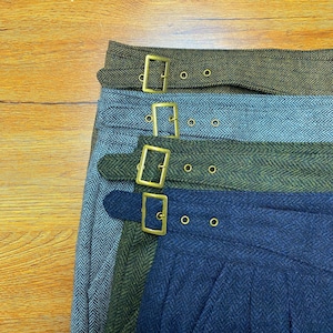May include: Four different fabric belts with gold metal buckles. The belts are layered on top of each other, with the top belt being a dark green and brown herringbone pattern, the second belt being a light blue herringbone pattern, the third belt being a dark green and brown herringbone pattern, and the bottom belt being a dark blue herringbone pattern.