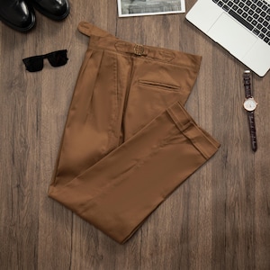 May include: A pair of brown twill pants with a belt loop and a single back pocket. The pants are folded in half and laid flat on a wooden surface.