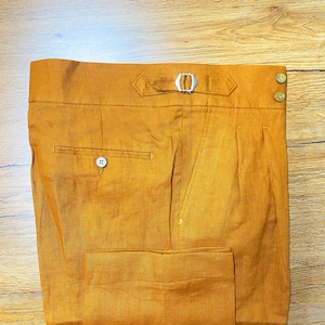 May include: A pair of mustard yellow linen pants with a belt loop and a single button pocket on the right side.