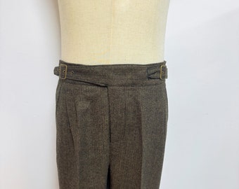 May include: Brown herringbone trousers with a brown leather belt with brass buckles.
