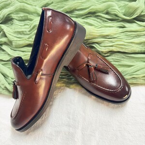 May include: A pair of brown leather tassel loafers. The loafers have a slip-on design and a pointed toe.