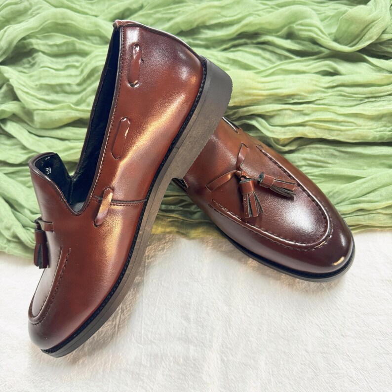 May include: A pair of brown leather tassel loafers. The loafers have a slip-on design and a pointed toe.